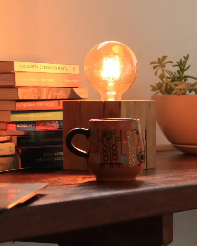 Mesa com livros, abajur aceso e caneca