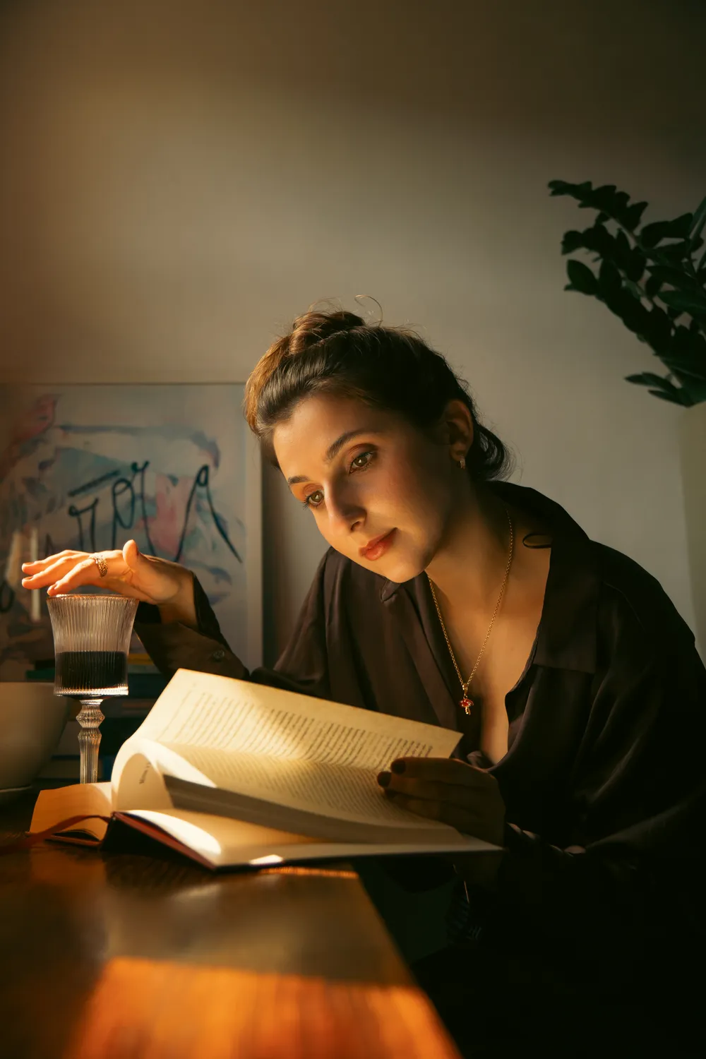 Isabela Vicarpi lendo um livro à mesa, sob luz quente